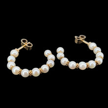 Load image into Gallery viewer, A pair of yellow gold pearl half hoop earrings with butterfly fittings, on a black background
