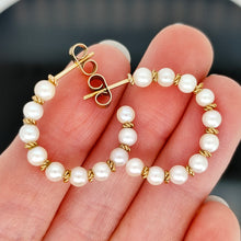 Load image into Gallery viewer, A pair of yellow gold pearl half hoop earrings with butterfly fittings, held in a hand
