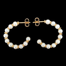 Load image into Gallery viewer, A pair of yellow gold pearl half hoop earrings with butterfly fittings, on a black background
