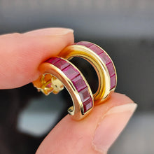 Load image into Gallery viewer, A pair of yellow gold hoop earrings channel set with square cut rubies held in a hand
