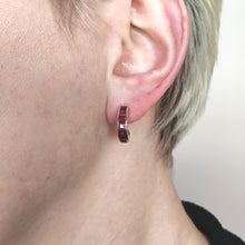 Load image into Gallery viewer, A yellow gold hoop earring channel set with square cut rubies, modelled in an ear
