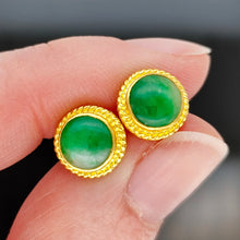 Load image into Gallery viewer, A pair of round jade stud earrings in yellow gold, held in a hand
