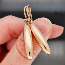 Load image into Gallery viewer, A pair of rose gold elongated drop earrings with hook fittings, held in a hand
