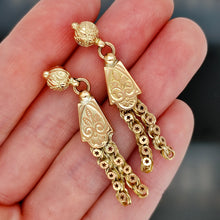 Load image into Gallery viewer, A pair of yellow gold fancy engraved tassel drop earrings, held in a hand
