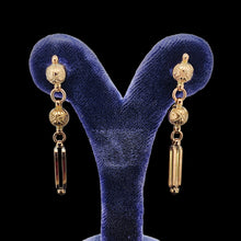 Load image into Gallery viewer, A pair of engraved bead and bar drop earrings in yellow gold, in an earring stand
