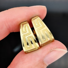 Load image into Gallery viewer, A pair of yellow gold Greek key design half hoop earrings, held between fingers
