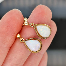 Load image into Gallery viewer, A pair of pear shaped opal drop earrings in yellow gold, held in a hand

