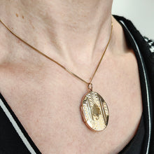 Load image into Gallery viewer, An oval yellow gold locket pendant with engraving, modelled around a neck, with a gold chain
