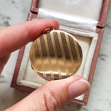 Load image into Gallery viewer, A circular yellow gold locket with pinstripe engraving, held in a hand
