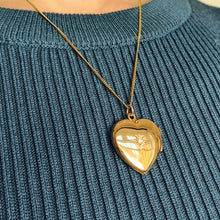 Load image into Gallery viewer, A yellow gold heart shaped locket with a diamond, modelled with a chain by a woman wearing a blue top
