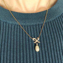 Load image into Gallery viewer, A yellow and white gold pearl and diamond bow pendant necklace, modelled by a woman wearing a blue top
