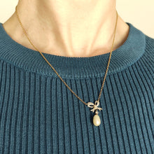 Load image into Gallery viewer, A yellow and white gold pearl and diamond bow pendant necklace, modelled by a woman wearing a blue top
