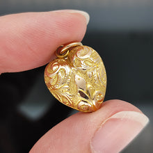 Load image into Gallery viewer, A yellow gold engraved heart shaped charm pendant, held between fingers
