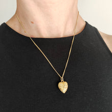 Load image into Gallery viewer, A yellow gold engraved heart shaped charm pendant, with a chain, modelled by a woman wearing a black top
