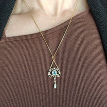 Load image into Gallery viewer, An aquamarine and pearl drop pendant in yellow gold, with a chain, modelled by a woman wearing a brown top
