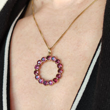 Load image into Gallery viewer, A circular yellow gold pendant with almandine garnets, modelled with a gold chain by a woman wearing a black and white dress
