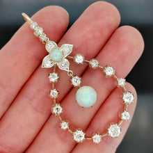 Load image into Gallery viewer, A pear shaped open pendant set with opals and diamonds, in gold and silver, held in a hand
