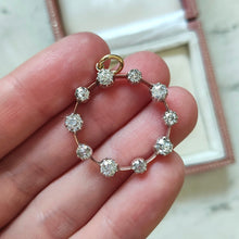 Load image into Gallery viewer, A ten stone old cut diamond open circle pendant in silver and gold, held in a hand
