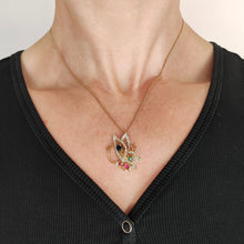 Load image into Gallery viewer, A yellow gold butterfly pendant with diamonds, rubies, a sapphire and an emerald, with a gold curb chain, modelled by a woman
