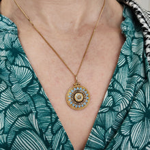 Load image into Gallery viewer, An antique pendant in yellow gold with seed pearls and light blue enamel, modelled with a chain by a woman wearing a green patterned top
