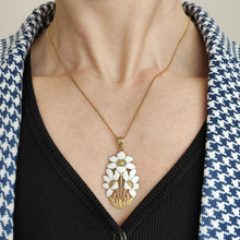 Load image into Gallery viewer, A white enamelled flower pendant, with a gold chain, modelled by a women
