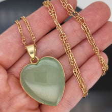 Load image into Gallery viewer, Heart-shaped green jade pendant on a gold chain held in a hand
