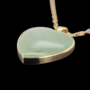 Heart-shaped jade pendant with gold edge on a black background