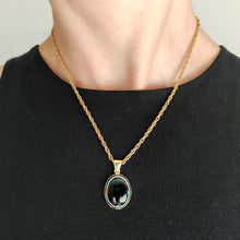 Load image into Gallery viewer, An oval banded agate pendant rubover set in yellow gold, with a yellow gold chain, modelled by a woman wearing a black top
