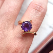 Load image into Gallery viewer, Gold ring with an amethyst on a finger against a neutral background
