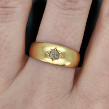 Load image into Gallery viewer, A solitaire old cut diamond gypsy set ring in yellow gold, modelled on the middle finger of a hand, on a black background
