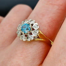 Load image into Gallery viewer, A blue zircon and diamond flower cluster ring in yellow and white gold, modelled on a hand
