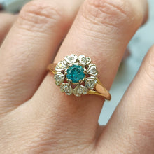 Load image into Gallery viewer, A blue zircon and diamond flower cluster ring in yellow and white gold, modelled on a hand
