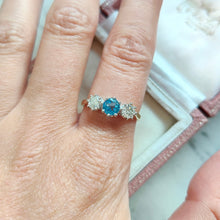 Load image into Gallery viewer, A three stone blue zircon and diamond ring in yellow and white gold, modelled on a hand

