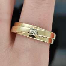 Load image into Gallery viewer, A yellow gold solitaire square cut diamond band, modelled on the index finger of a hand, on a black background
