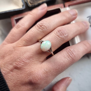 Hand wearing a ring with an opal on a neutral background