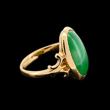 Load image into Gallery viewer, An oval shaped green jade ring in yellow gold, on a black background
