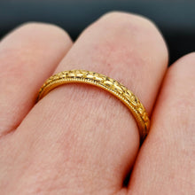 Load image into Gallery viewer, A yellow gold floral patterned wedding band ring, modelled on a hand
