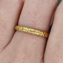 Load image into Gallery viewer, A yellow gold floral patterned wedding band ring, modelled on a hand
