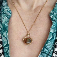 Load image into Gallery viewer, An oval spinner fob pendant in yellow gold with agate, on a chain, modelled by a woman wearing a green patterned top
