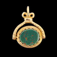 Load image into Gallery viewer, An oval spinner fob pendant in yellow gold with bloodstone, on a black background
